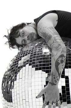 a man with tattoos laying on top of a large mirror ball in black and white