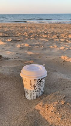 a cup of coffee sitting on top of a sandy beach