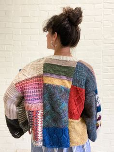 a woman standing in front of a white brick wall wearing a multicolored sweater