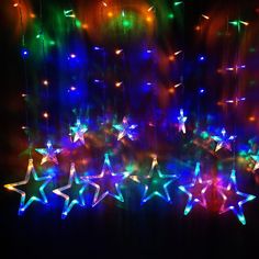 multicolored stars are hanging from strings in the dark, with lights shining on them