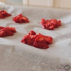 small pieces of red fruit sitting on top of a white table cloth covered in wax paper