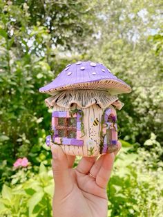 a hand holding up a small purple mushroom house