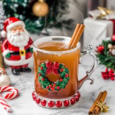 a glass mug filled with hot chocolate and cinnamon on top of a table next to christmas decorations