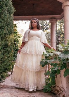 a woman in a white dress standing on a stone walkway with greenery around her