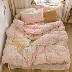 an unmade bed with pink and white comforter in front of a small window