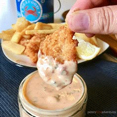 a person dipping some kind of food into a small glass jar with sauce on it