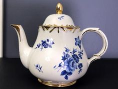 a white tea pot with blue flowers painted on the side and gold trimmings