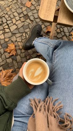 a person holding a cup of coffee in their hand while sitting on a park bench