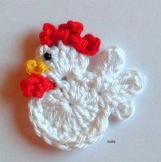 a crocheted chicken brooch is shown on a white surface with red and yellow flowers