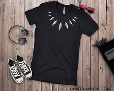 Take your rightful place as King of Wakanda with this cool Black Panther t shirt. Inspired by the Black Panther costume, these tees make a great gift for superhero fans of all ages. Available in Mens, Ladies and Youth sizes. All of these tops are fabric laundered for reduced shrinkage. Ladies sizes are slim fit and may feel smaller than styles you are used to. Consider a size up for a looser fit. PLEASE REFER TO THE SIZING CHARTS IN THE PICS BEFORE CHOOSING A SIZE! Be sure to check out Brandy's Black Panther Necklace, Superhero Tshirt, Panther Necklace, Panther Costume, Panther Shirt, Black Panther Shirt, Black Panther Costume, Black Panther T Shirt, African Shirt