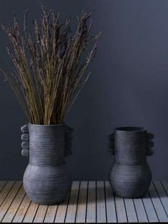 two gray vases sitting on top of a wooden table with dried plants in them