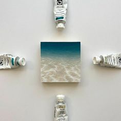 four bottles are arranged in the shape of squares on a white surface with water and sand