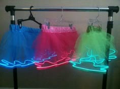 two skirts with neon lights on them hanging from a clothes rack in front of a wall