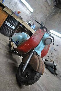 an old red and blue motorcycle parked in a garage next to a pile of junk