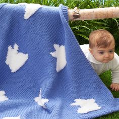 a baby crawling under a blanket on the ground in front of some grass and trees