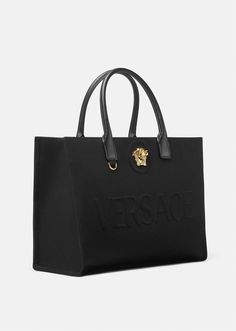 Crafted in tonal canvas with leather top handles, this classic tote bag is adorned with a Medusa plaque and raised Versace logo lettering. The roomy interior has a large zipped pocket and protector strap. Attach a Versace bag charm with the D-ring for an added touch of style. Luxury Logo Bags, Versace Virtus Top Handle Bag, Versace Travel Bag, Luxary Handbags, Luxury Shopping Bags, Versace Womens, Versace Bag, Womens Designer Bags, Versace Bags