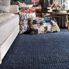 a living room filled with lots of pillows and blankets on top of a blue rug