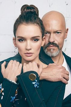 a man and woman standing next to each other in front of a white brick wall