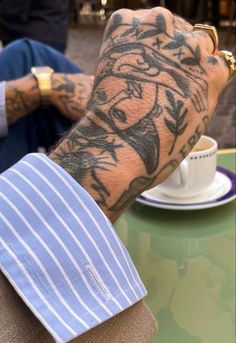 a tattooed arm sitting on top of a table next to a cup and saucer