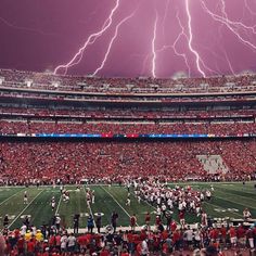 lightning strikes in the sky over a football stadium full of fans and players during a game