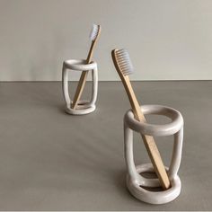 two toothbrush holders made out of white ceramic and wood, each holding a bamboo toothbrush