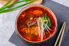 a wooden bowl filled with soup next to chopsticks on top of a table