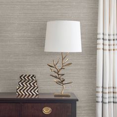 a lamp on top of a wooden dresser next to a white and black striped curtain