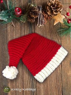 a red and white knitted hat sitting on top of a wooden table next to pine cones