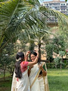 two women standing next to each other near a palm tree