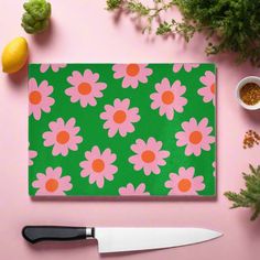 a pink and green flowered cutting board next to a knife on top of a table