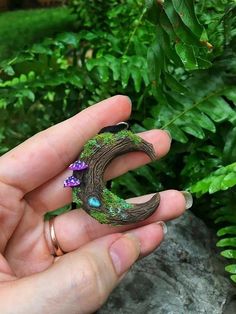 a person holding a ring in their hand with green plants behind it and purple flowers on the outside