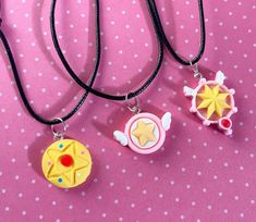 three necklaces with different designs on them sitting on a pink tableclothed surface