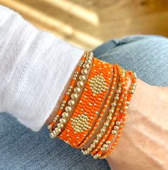 an orange beaded bracelet is on someone's arm and it has gold beads