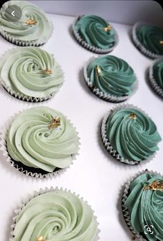 cupcakes with green frosting and gold decorations on them in a white box