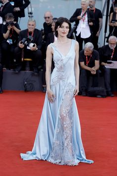 a woman in a blue gown standing on a red carpet with cameras around her and people taking pictures