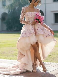 a woman in a pink dress is standing on a brick walkway and holding a bouquet of flowers