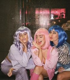 three women sitting next to each other in front of a window with pink and blue hair