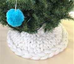 a knitted christmas tree ornament hanging from a pine tree branch with blue pom - poms