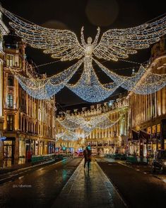 a person walking down a street with christmas lights hanging from the ceiling and buildings in the background