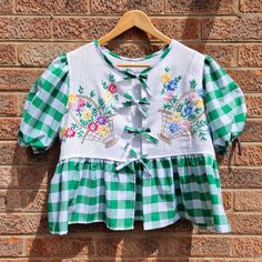 a green and white checkered shirt with flowers on it hanging against a brick wall