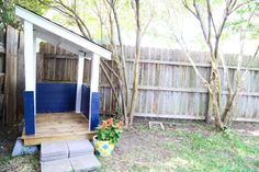 a small wooden shed with blue doors in the back yard next to a tree and fence