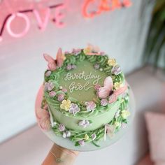 a hand holding a green birthday cake with butterflies on it and the words love cake