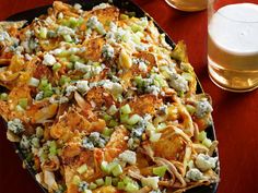 a platter filled with nachos next to two glasses of beer