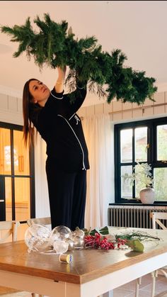 a woman standing on top of a wooden table holding onto a christmas tree over her head