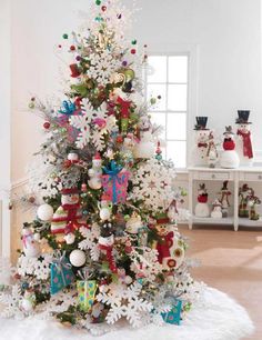 a white christmas tree with snowflakes, ornaments and bows on it in a living room