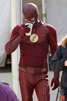 a man dressed as the flash drinking from a cup while standing next to a woman