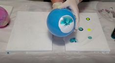 a person in white gloves is painting a blue ball on a table with other items