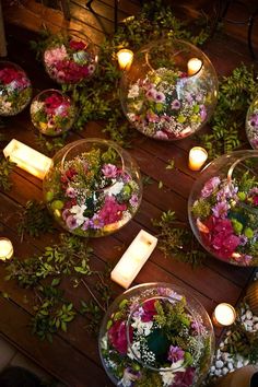 flowers and candles are arranged in glass bowls on a wooden table surrounded by greenery