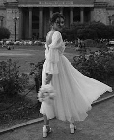 a woman in a long white dress is walking down the street with her hand on her hip