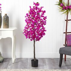 a purple tree in a black pot next to a white chair and table with vases on it